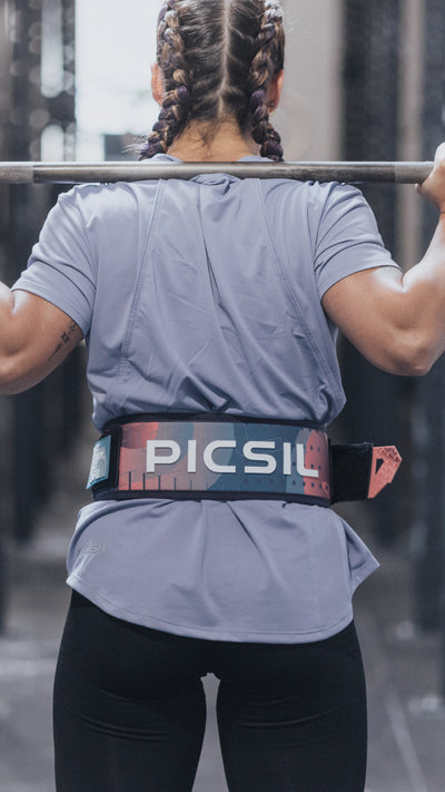 Atleta femenina de espaldas levantando barra en gimnasio, usando cinturón lumbar para entrenamientos de crosstraining y halterofilia