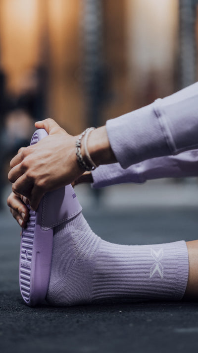 Persona estirando la pierna en el suelo con chanclas y calcetines color lila